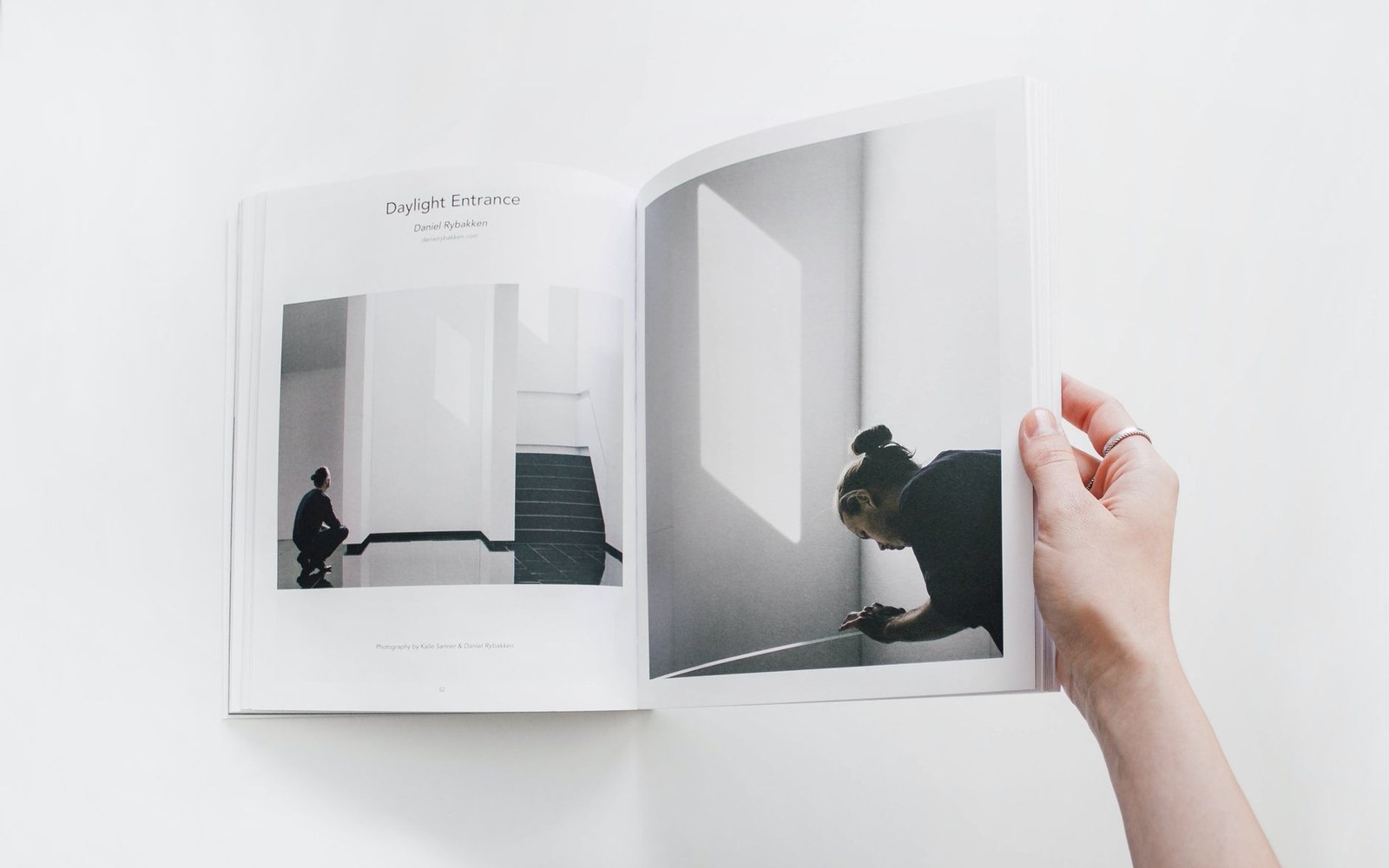 A hand turns a page of an open magazine featuring photos of a figure in a sunlit hallway