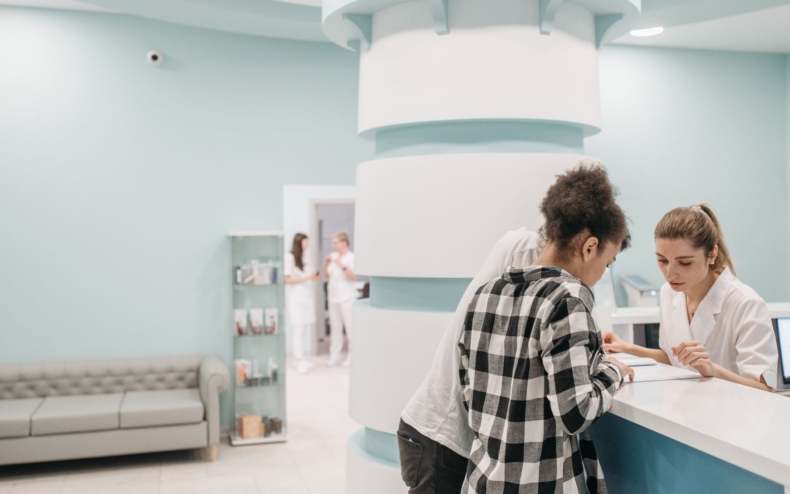 A receptionist in a white coat assists a client at a clinic front desk