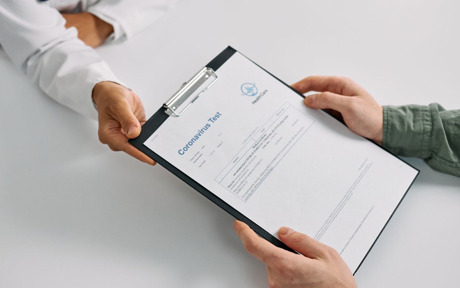 A doctor hands a patient a clipboard holding a coronavirus test form