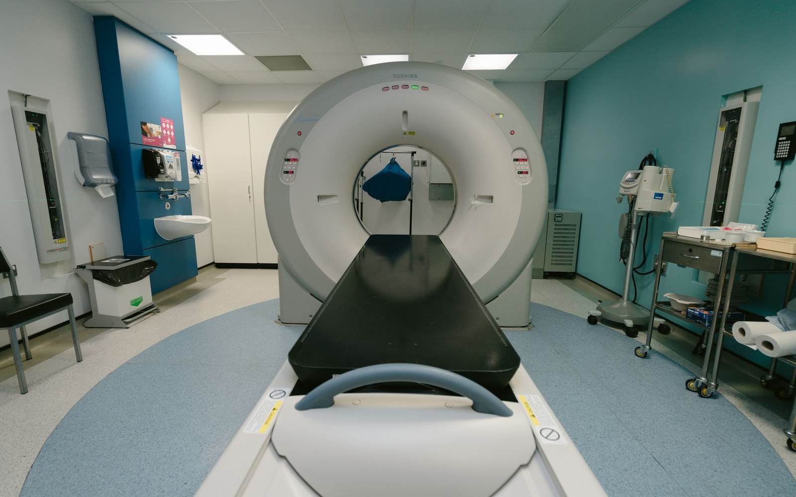 An empty MRI scanner room with the patient table extended in front of the machine